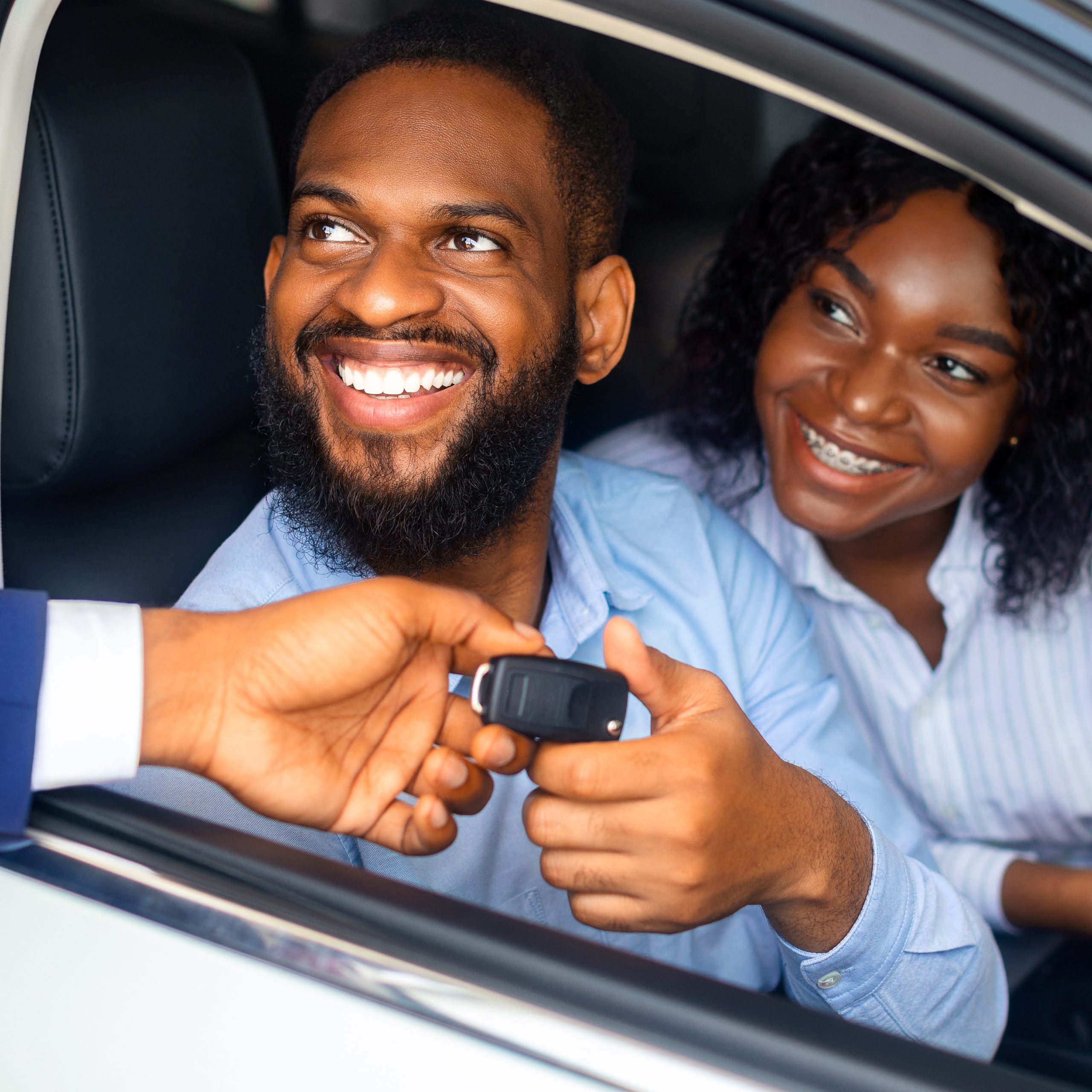 Happy African American Couple Taking Key From Salesman After Buying New Car In Dealership Center, Cheerful Black Spouses Sitting In Their Automobile And Smiling Through Window, Closeup Shot
